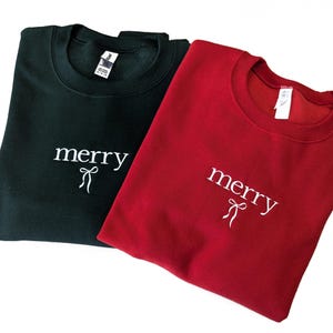 Könnte beinhalten: Zwei Sweatshirts, eines grün und eines rot, mit dem Wort "merry" und einer Schleife, die auf der Vorderseite gestickt ist.