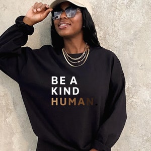 May include: A black sweatshirt with the text "BE A KIND HUMAN." in white and gold lettering.