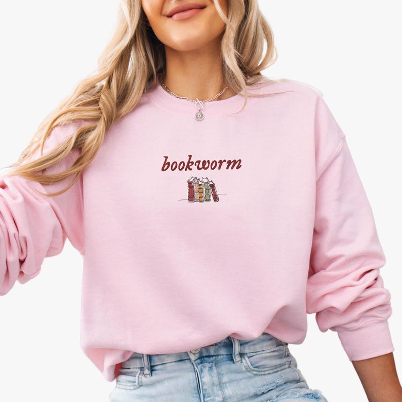 May include: A pink sweatshirt with the text "bookworm" in maroon lettering and a small illustration of a stack of books.