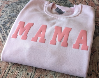 May include: A pink sweatshirt with the word "MAMA" printed in a large, bold, pink font.