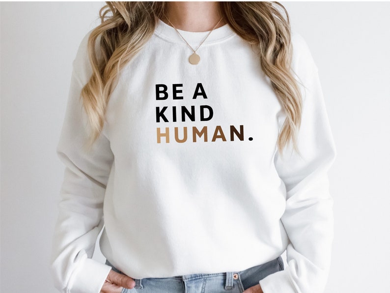 May include: White sweatshirt with the text "BE A KIND HUMAN." in black and gold lettering.