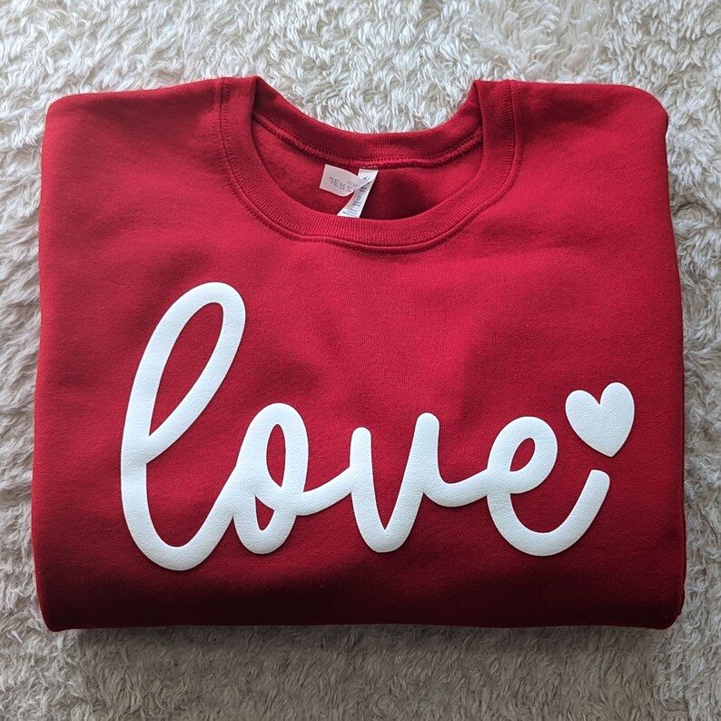 May include: Red sweatshirt with a white cursive "love" with a small white heart.