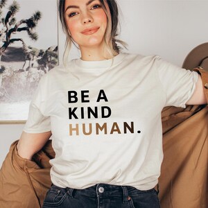 May include: A white t-shirt with the text "BE A KIND HUMAN." printed in black and brown.
