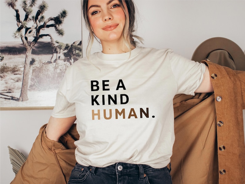 May include: A white t-shirt with the text "BE A KIND HUMAN." printed in black and brown.