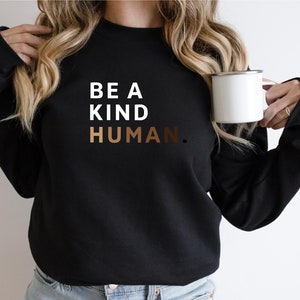 May include: A black sweatshirt with the text "BE A KIND HUMAN." in white and brown lettering.