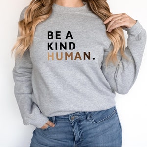 May include: A grey sweatshirt with the text "BE A KIND HUMAN." printed in black and brown.