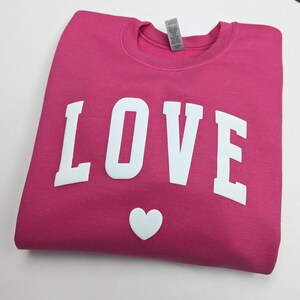 May include: A pink sweatshirt with the word "LOVE" printed in white on the front. A white heart is below the word.