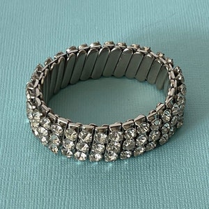 May include: A silver expandable bracelet with three rows of clear rhinestones.
