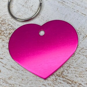 May include: A bright pink heart-shaped metal tag with a silver key ring. The tag has a hole in the top for attaching to a key chain.