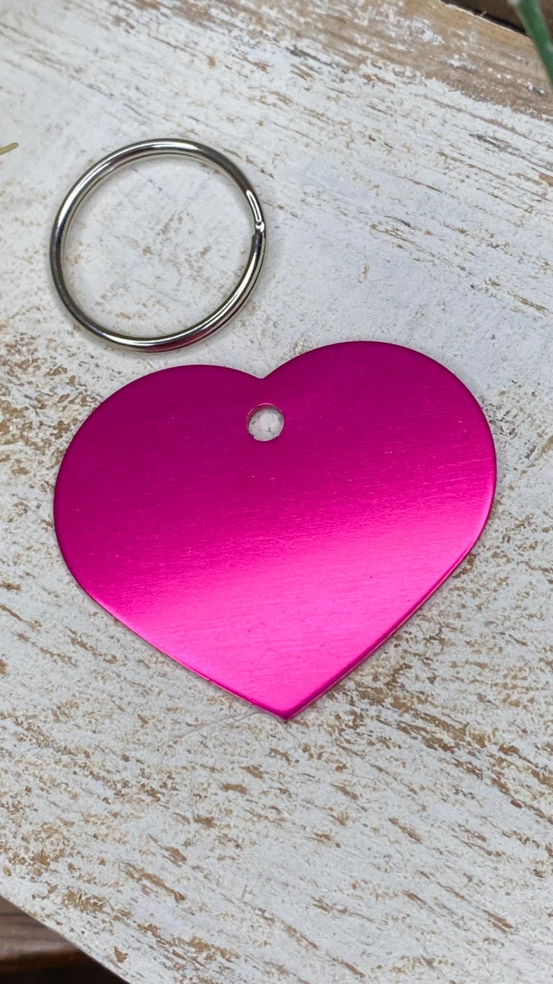 May include: A bright pink heart-shaped metal tag with a silver key ring. The tag has a hole in the top for attaching to a key chain.