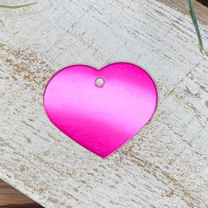 May include: A bright pink heart-shaped metal tag with a hole at the top.