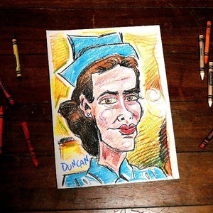 Puede incluir: Un dibujo colorido de una persona con cabello castaño que lleva un sombrero azul y una camisa azul. El dibujo está en papel blanco con la palabra "Duncan" escrita en azul en la parte inferior.