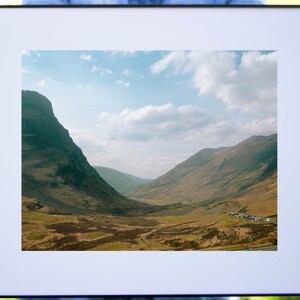 May include: A framed photograph of a valley in the Scottish Highlands. The valley is surrounded by green hills and a blue sky with white clouds.