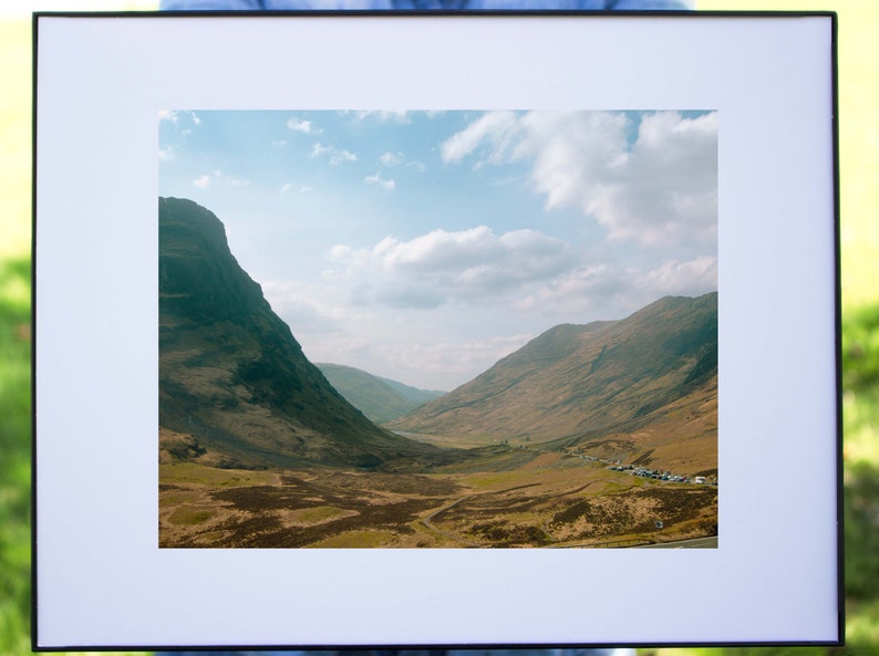 May include: A framed photograph of a valley in the Scottish Highlands. The valley is surrounded by green hills and a blue sky with white clouds.