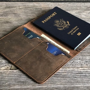 May include: A brown leather passport holder with two card slots and a pocket for cash. The holder is open and a blue US passport is visible inside.