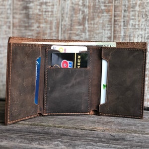 May include: A brown leather trifold wallet with multiple card slots and a cash pocket. The wallet is open and shows the interior with several cards inserted.
