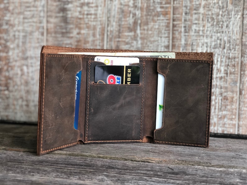 May include: A brown leather trifold wallet with multiple card slots and a cash pocket. The wallet is open and shows the interior with several cards inserted.
