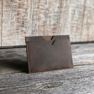 K&ouml;nnte beinhalten: Ein brauner Lederkartenhalter mit zwei F&auml;chern. Der Halter ist aus verwittertem Leder und hat einen rustikalen Look.
