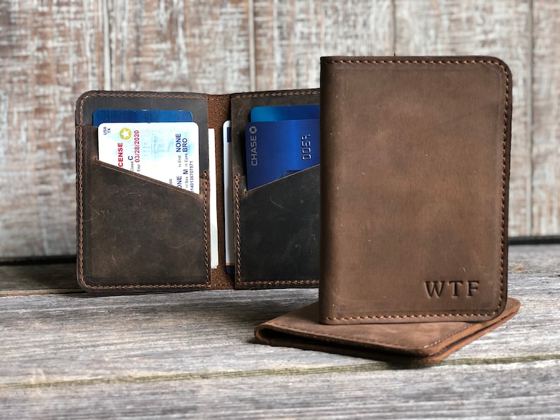 May include: Two brown leather wallets with a stitched edge. The wallet on the left has a blue driver's license and a credit card inside. The wallet on the right has the initials "WTF" embossed on the front.