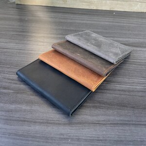 May include: Four leather wallets stacked on top of each other. The top wallet is gray, the second is brown, the third is brown with a lighter shade, and the bottom wallet is black.