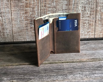 May include: A brown leather wallet with multiple card slots and a cash pocket. The wallet is open and shows a credit card, a driver's license, and cash.