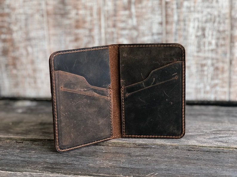 May include: A brown leather wallet with multiple pockets and a stitched edge. The wallet is open and the inside is visible.