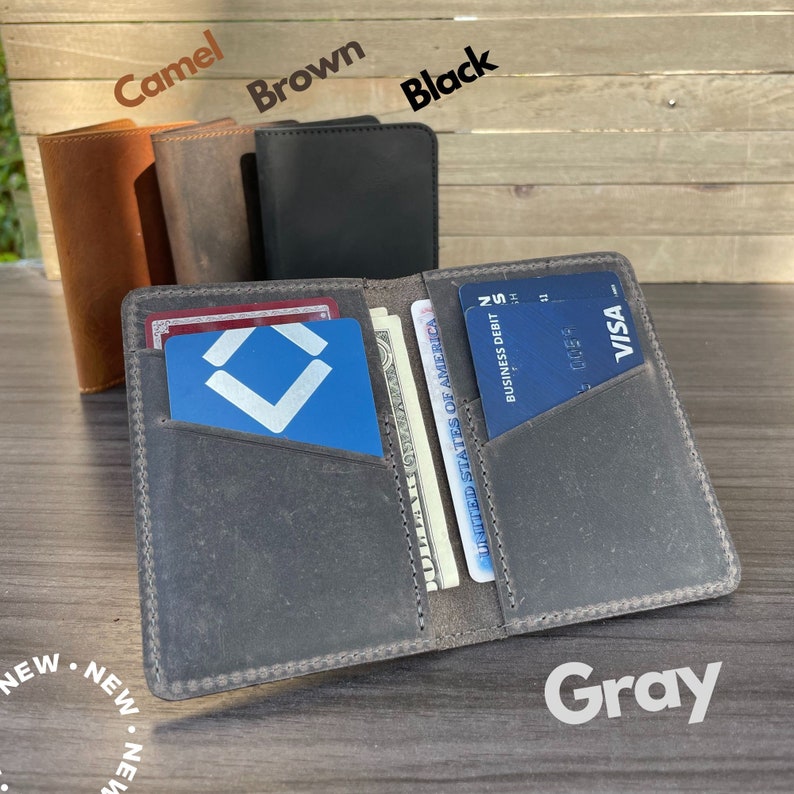 May include: A gray leather wallet with multiple card slots and a cash pocket. The wallet is open and shows a blue card with a white logo, a US dollar bill, and a credit card with the VISA logo.