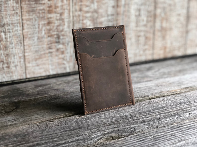 K&ouml;nnte beinhalten: Eine braune Ledergeldb&ouml;rse mit mehreren Kartenf&auml;chern und einem gro&szlig;en Fach. Die Geldb&ouml;rse hat einen Used-Look und ist mit braunem Garn vern&auml;ht.