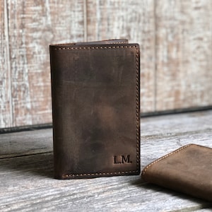 May include: Two brown leather wallets with a distressed finish. The wallet on the left has the initials "L.M." embossed on the front.