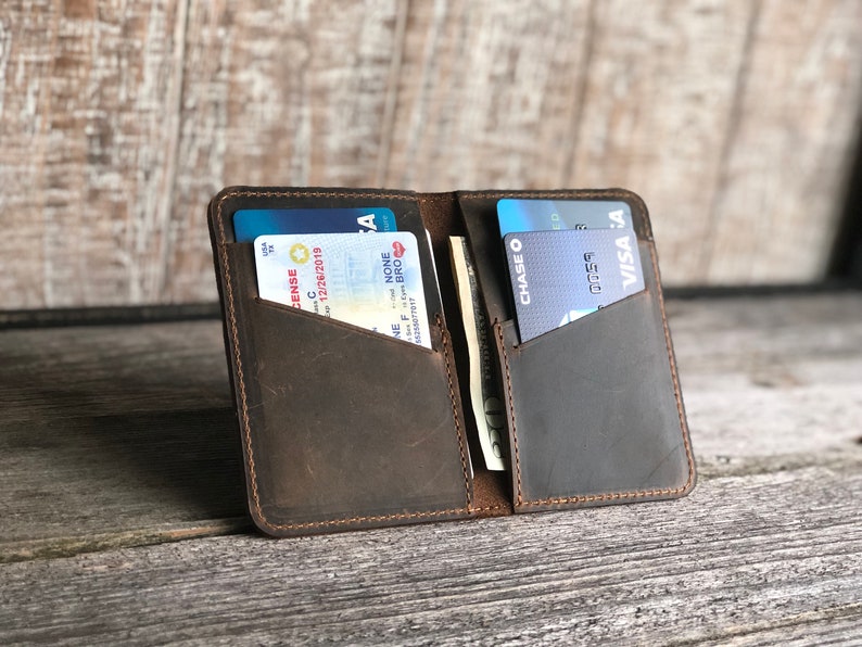 May include: A brown leather wallet with two card slots and a cash pocket. The wallet is open and has a driver's license, credit cards, and cash inside.
