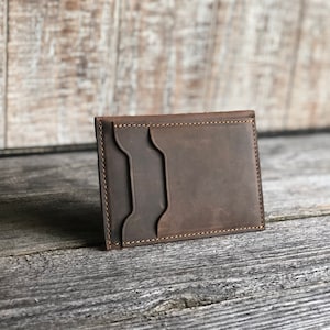 K&ouml;nnte beinhalten: Eine braune Ledergeldb&ouml;rse mit einem gen&auml;hten Rand und zwei Kartenf&auml;chern.
