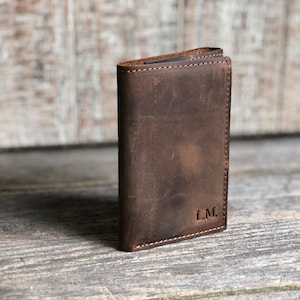 May include: A brown leather wallet with a stitched edge and the initials "L.M." embossed on the front.