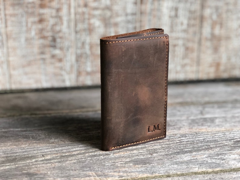 May include: A brown leather wallet with a stitched edge and the initials "L.M." embossed on the front.