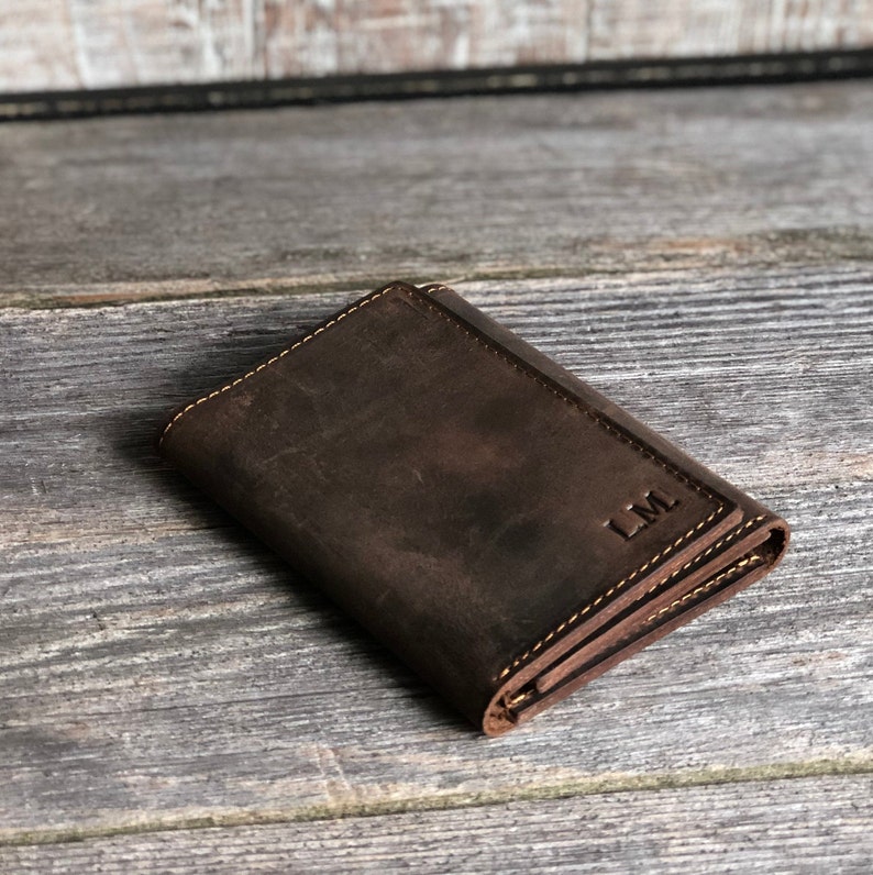 May include: A brown leather wallet with a fold-over closure and a monogrammed "LM" on the front.
