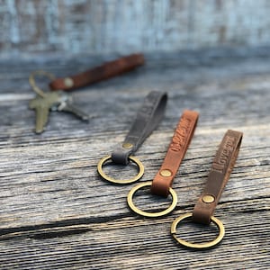 Personalized slim leather keychains pictured. Handmade keychains come in six colors: Tan, Gray, Brown and Red (Burgundy), Black (not shown), and Light Brown. 1/4” wide and 4 1/2” long slim design leather keychains on the picture. Made in USA!