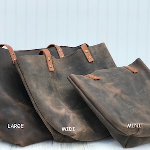 May include: Three dark brown leather tote bags in large, midi, and mini sizes. Each bag features tan leather straps secured with metallic rivets. The bags are labeled with the text LARGE, MIDI, and MINI printed in white on the surface below each bag.