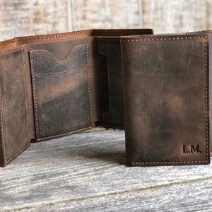 May include: A brown leather trifold wallet with a stitched edge and the initials "L.M." embossed on the front.