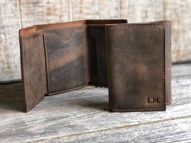 May include: A brown leather trifold wallet with a stitched edge and the initials "L.M." embossed on the front.