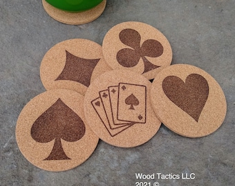 May include: A collection of round cork coasters with playing card suit designs: spades, diamonds, clubs, and hearts. One coaster features a hand of cards. A green mug sits on a matching coaster. The coasters are a light brown color.