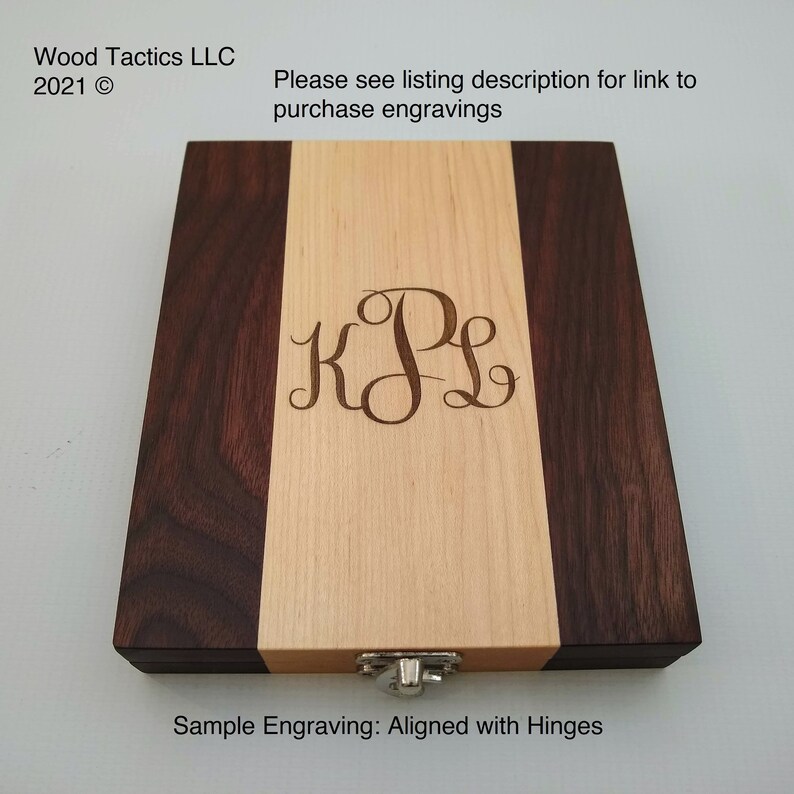 May include: A wooden box with a walnut and maple wood grain pattern. The box has a hinged lid and a metal latch. The box is engraved with the initials "KPL" and the text "Sample Engraving: Aligned with Hinges".