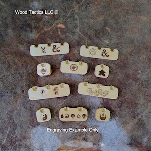 May include: Engraved wooden dice trays and tokens with various symbols and numbers. The trays are designed to hold dice for role-playing games. The tokens are numbered and feature different symbols, including a yin-yang symbol, a dragon, and a skull.