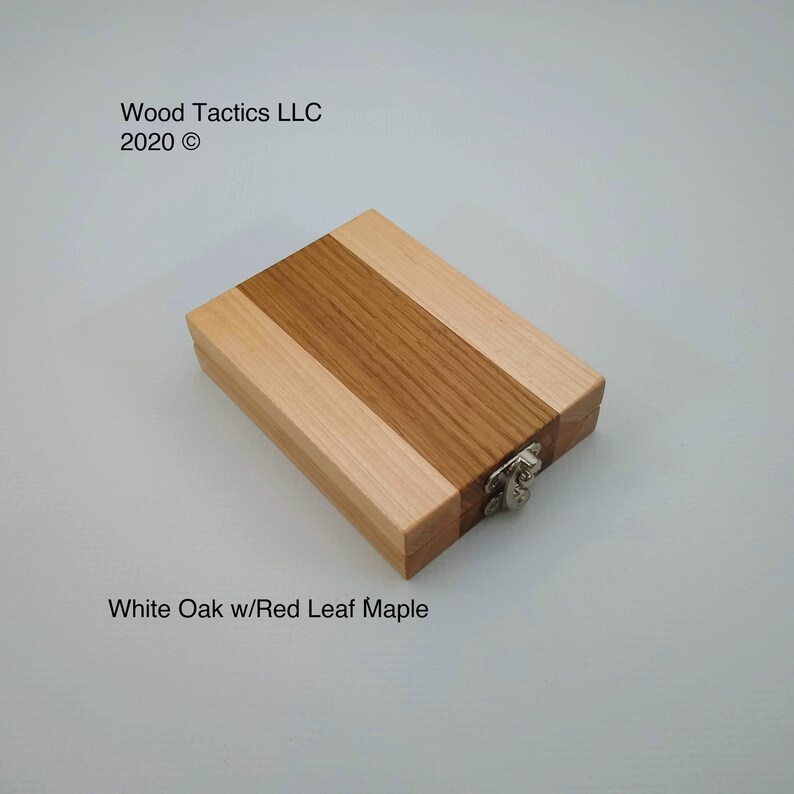 May include: A small wooden box with a hinged lid and a metal clasp. The box is made from two types of wood: white oak and red leaf maple. The wood is arranged in alternating stripes.
