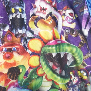 Puede incluir: Una tela con un fondo morado vibrante de tem&aacute;tica espacial que presenta un patr&oacute;n repetitivo de varios personajes de videojuegos, incluyendo una gran planta pira&ntilde;a verde con dientes blancos afilados, una criatura roja con corona y Bowser.
