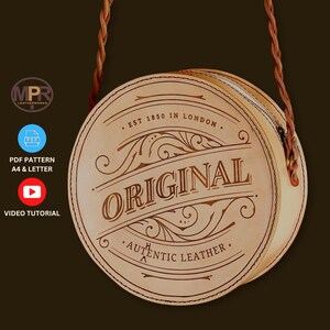 May include: A round, light brown leather handbag with a braided strap. The bag features the word "ORIGINAL" in a decorative font, along with "AUTHENTIC LEATHER" and "EST 1850 IN LONDON". A zipper closure is visible. The bag is a circle shape.