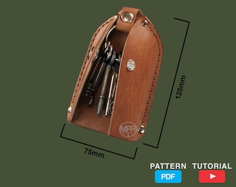 Puede incluir: Un llavero de cuero marrón con una solapa que se abre para revelar un llavero con varias llaves. El llavero mide 75 mm por 125 mm.  PATTERN TUTORIAL PDF y un icono de botón de reproducción también son visibles.