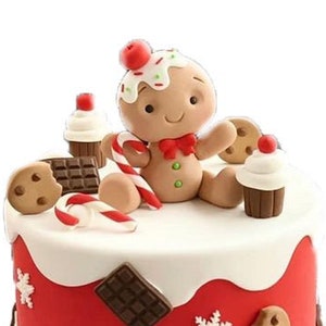 May include: A red and white Christmas cake decorated with gingerbread man, candy canes, chocolate, and cookies.