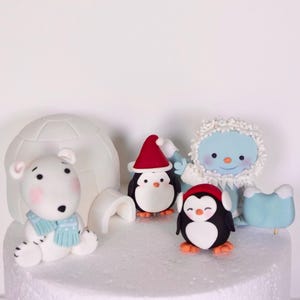 May include: A white cake decorated with fondant figures of a polar bear, a penguin wearing a Santa hat, a snowman, and another penguin wearing a red hat. The cake is also decorated with a white fondant igloo.