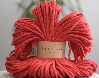 May include: A close-up of a large spool of red cotton rope. The rope is wrapped around itself and has a brown label that says "Bilibag Factory".