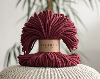 May include: A close-up of a large spool of deep red cotton rope. The rope is tightly wound and has a natural, rustic look. The spool is labeled "Bilibag Factory".