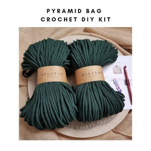 May include: A crochet DIY kit for making a pyramid bag. The kit includes two spools of dark green cotton rope, a crochet hook, and instructions. The rope is labeled "Bilibag Factory".